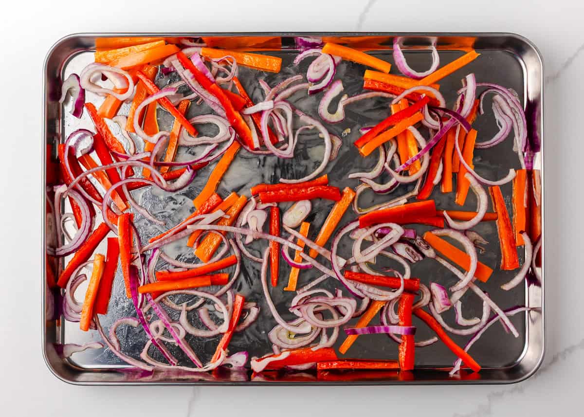 Colorful, fresh, and customizable, these chicken shawarma bowls are packed with bold spices, tender chicken, and all your favorite toppings. Bell peppers and red onion spread on a sheet pan for roasting.