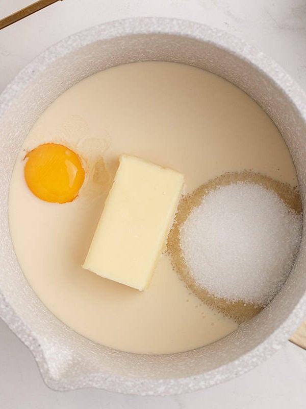 Butter, sugar, evaporated milk, and egg yolks cooking in a saucepan for coconut pecan frosting.