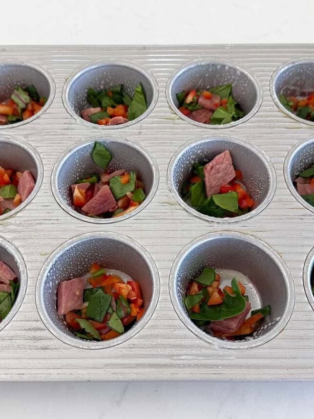 Muffin pan filled with chopped vegetables and ham for high protein cottage cheese egg bites.
