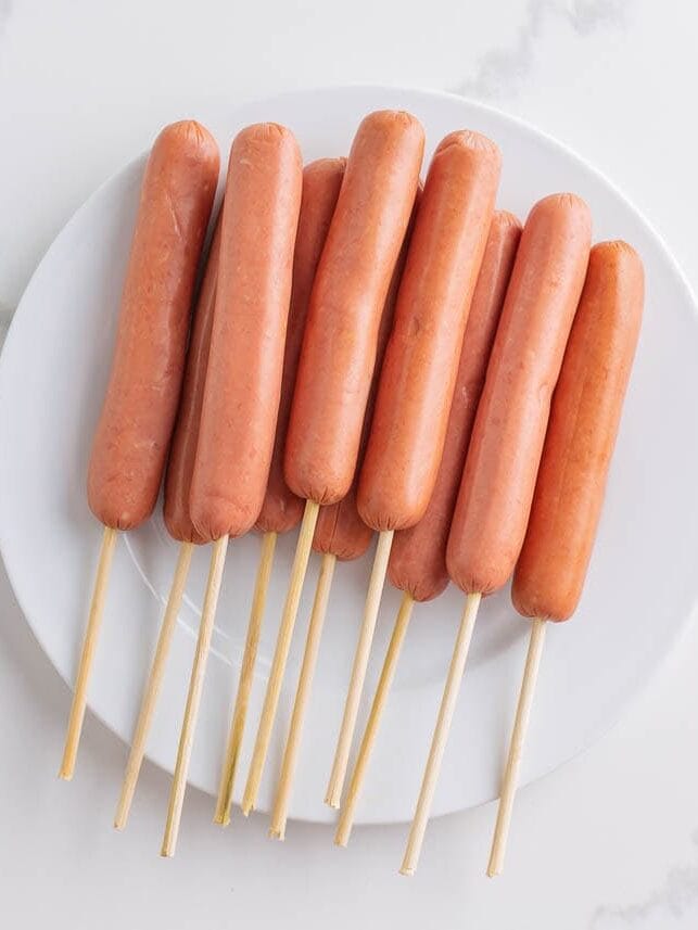 Hot dogs skewered on wooden sticks, ready to make corn dogs.
