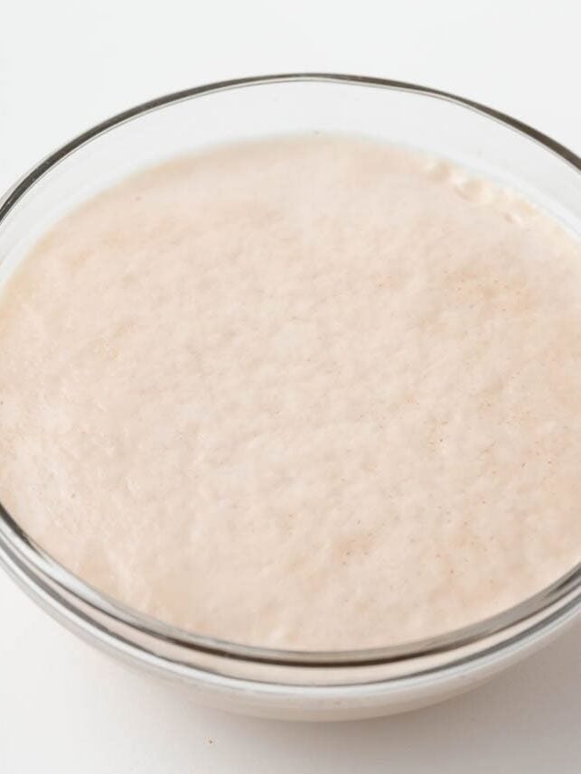 Active dry yeast dissolved in warm water and sugar, fully foamed and bubbly in a glass bowl.