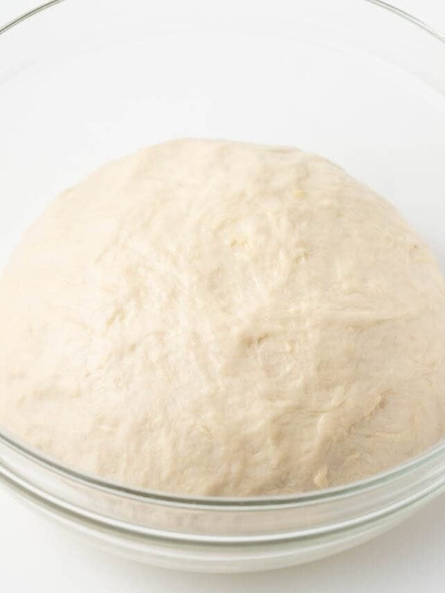 Pizza dough after rising, puffed and doubled in size in a glass bowl.