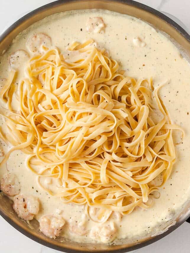 Cooked fettuccine noodles added to creamy alfredo sauce with shrimp.