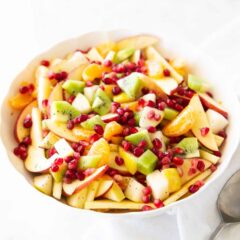 Colorful winter fruit salad featuring fresh apples, pears, kiwi, clementines, and pomegranate seeds in a honey citrus dressing.