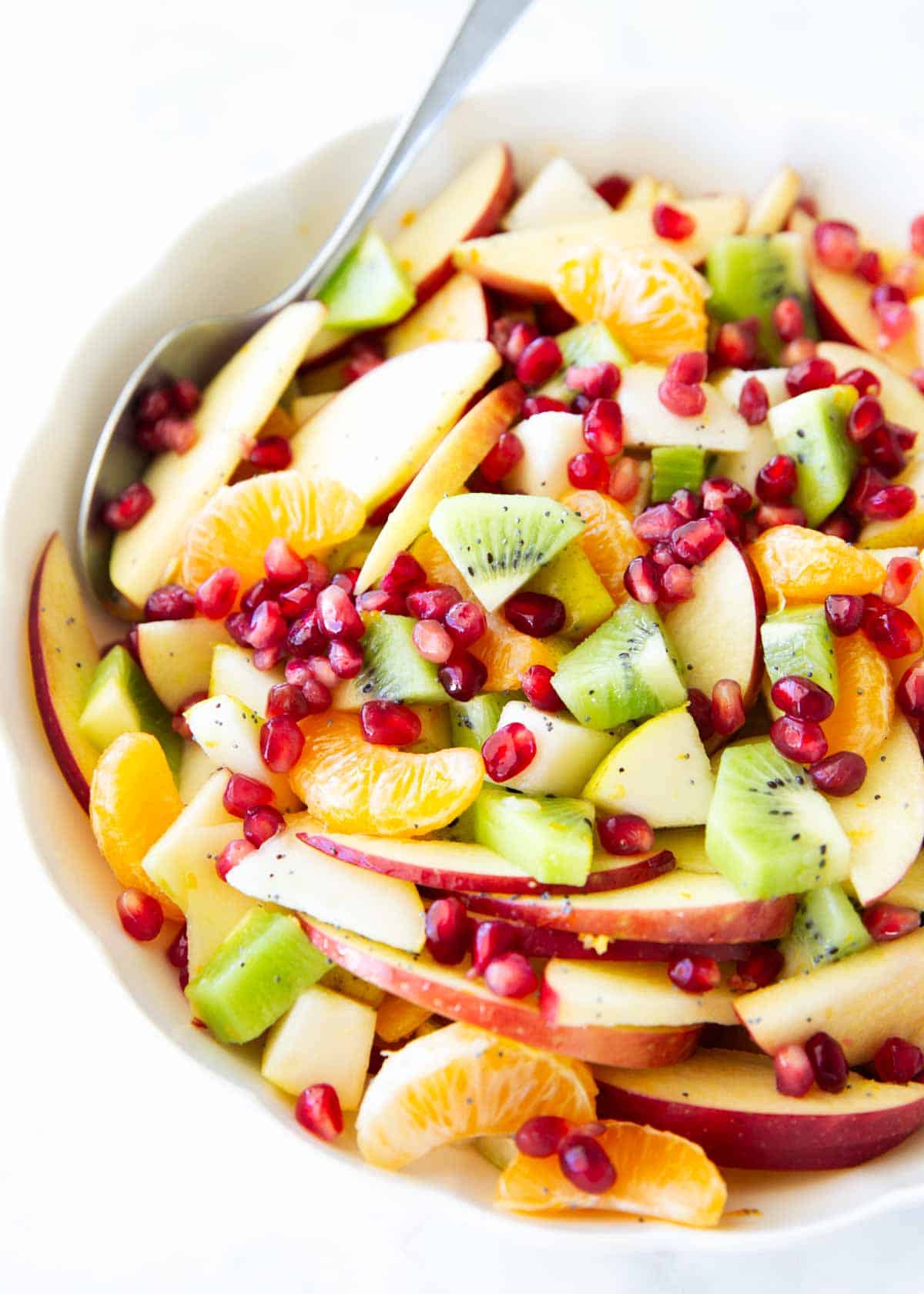 This winter fruit salad is made with apples, pears, kiwi, clementines, and pomegranate arils, then tossed in a light citrus honey dressing. An easy, fresh side dish ready in minutes! Overhead view of winter fruit salad with sliced apples, diced kiwi, peeled clementines, and citrus dressing in a white bowl.