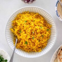 Overhead view of yellow rice served in a bowl with flatbread and hummus on the side.