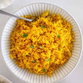 Bowl of yellow rice garnished with fresh herbs and ready to serve.