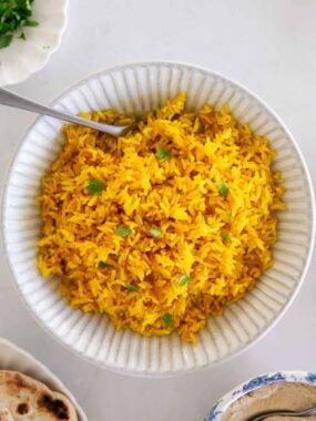 Bowl of yellow rice garnished with fresh herbs and ready to serve.