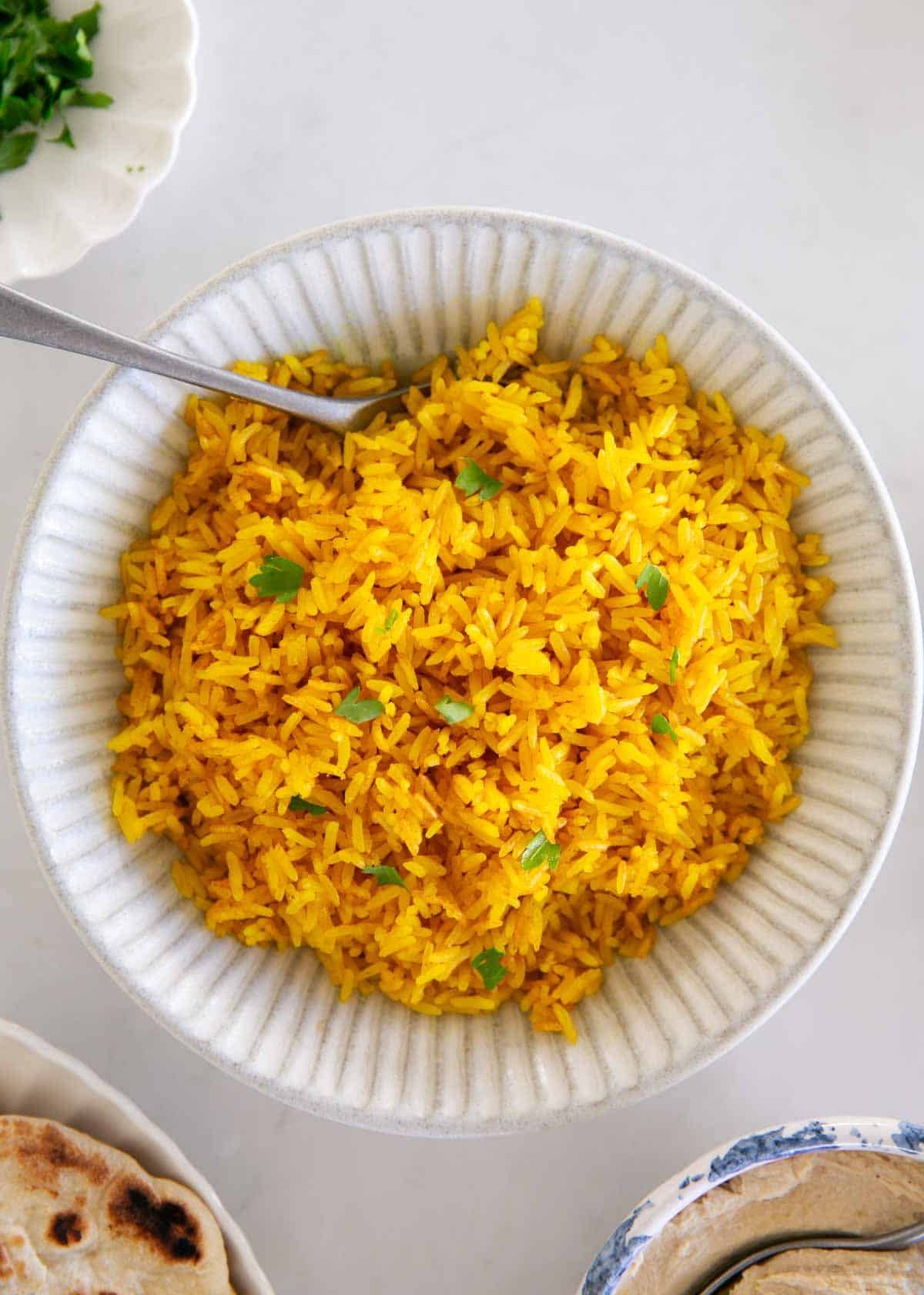This easy yellow rice is cooked on the stovetop with chicken broth and turmeric for a fluffy, flavorful side dish recipe that elevates any meal and is ready in only 25 minutes! Bowl of yellow rice garnished with fresh herbs and ready to serve.