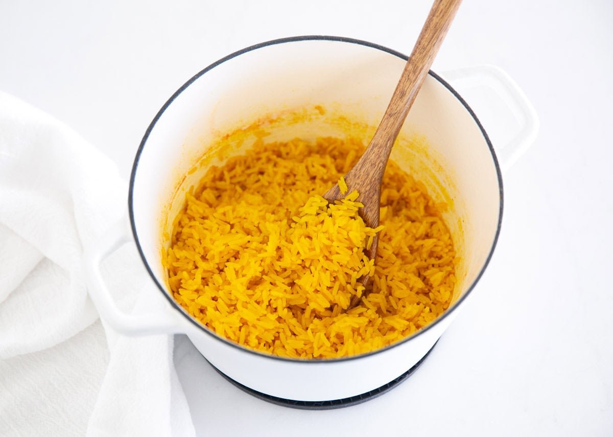 This easy yellow rice is cooked on the stovetop with chicken broth and turmeric for a fluffy, flavorful side dish recipe that elevates any meal and is ready in only 25 minutes! Fluffy yellow rice cooked in a white pot with a wooden spoon.
