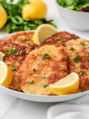 Golden brown chicken schnitzel with a crispy panko crust, garnished with parsley and lemon slices.