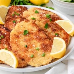 Crispy pan fried chicken schnitzel cutlets arranged on a plate with fresh parsley and lemon.