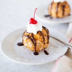 Fried ice cream topped with whipped cream, chocolate sauce, and a maraschino cherry.