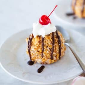 Close-up of fried ice cream with chocolate drizzle, whipped cream, and cherry on top.