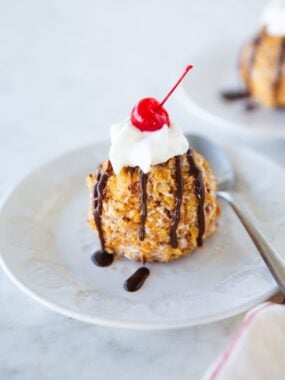 Close-up of fried ice cream with chocolate drizzle, whipped cream, and cherry on top.