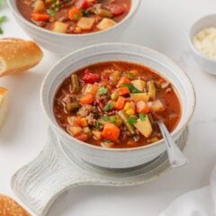 Hearty vegetable soup topped with fresh parsley served in a ceramic bowl.