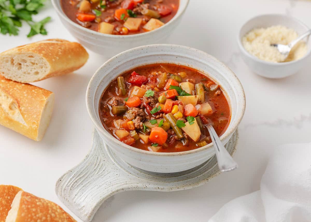 Hearty vegetable soup topped with fresh parsley served in a ceramic bowl.