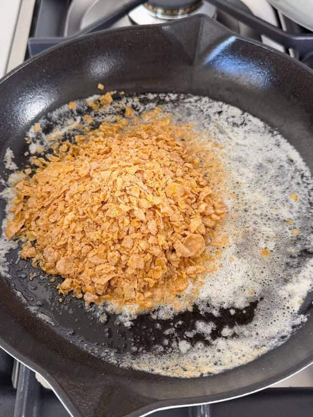 This fried ice cream recipe is made without deep frying, so it’s easy, mess-free, and just as crunchy as your favorite Mexican restaurant dessert. Crushed frosted flakes toasting in butter with cinnamon in a skillet for fried ice cream coating.