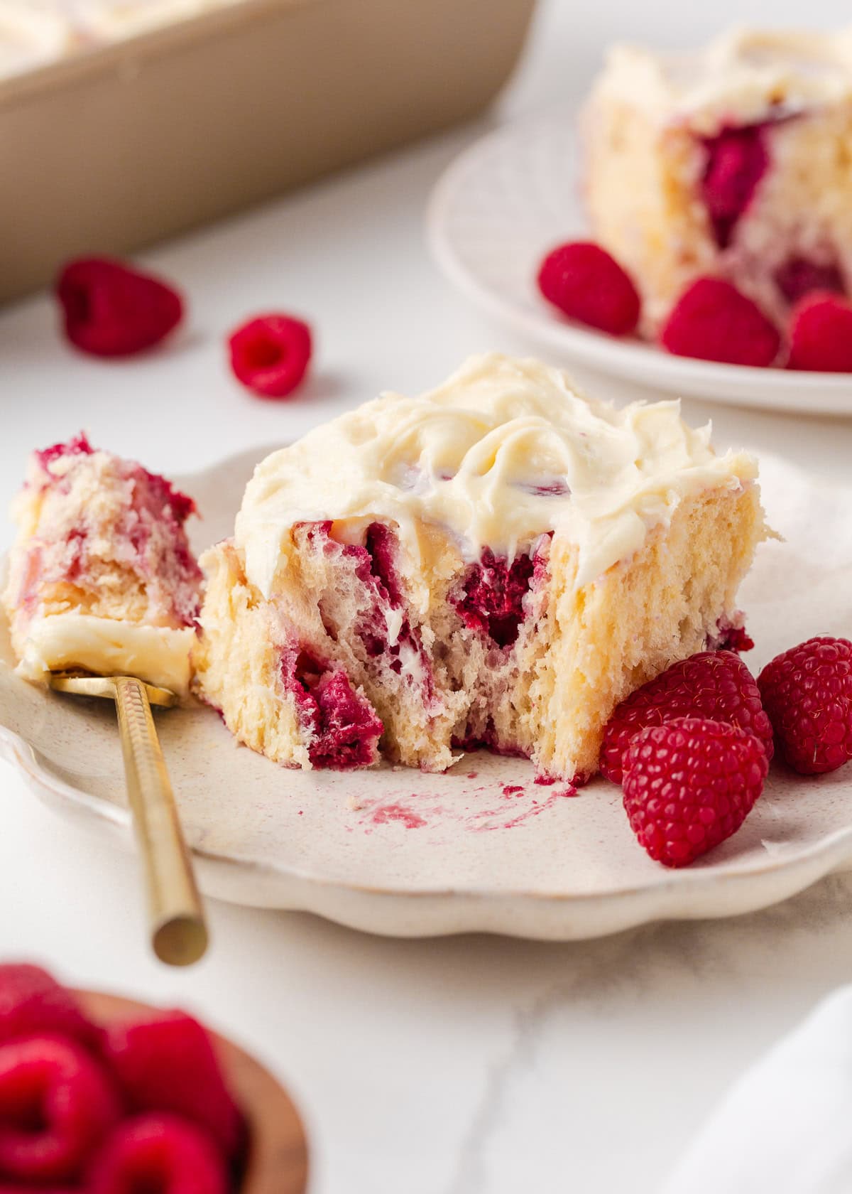 These raspberry sweet rolls are an indulgent breakfast treat made with soft yeast dough, a swirled frozen raspberry filling, and thick cream cheese frosting! Close up of raspberry sweet rolls topped with cream cheese frosting and fresh raspberries on a plate.