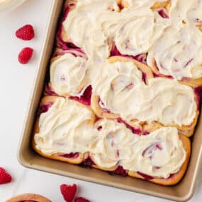 Raspberry sweet rolls topped with thick cream cheese icing in a baking pan.
