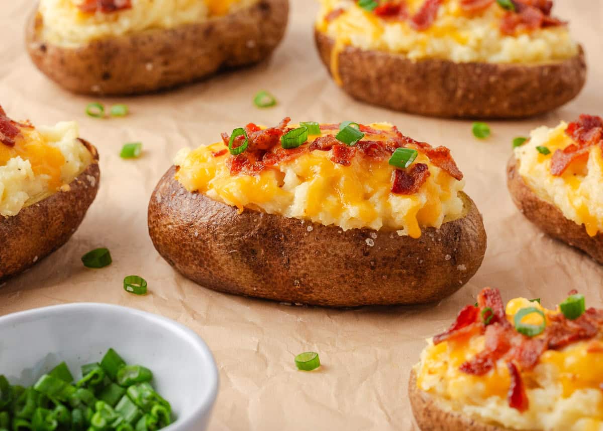 Cheesy twice baked potatoes with bacon and green onions arranged on parchment paper, ready to serve.