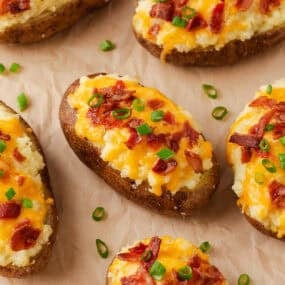 Oven baked twice baked potatoes filled with creamy mashed potatoes, cheddar cheese, and bacon, garnished with sliced green onions.