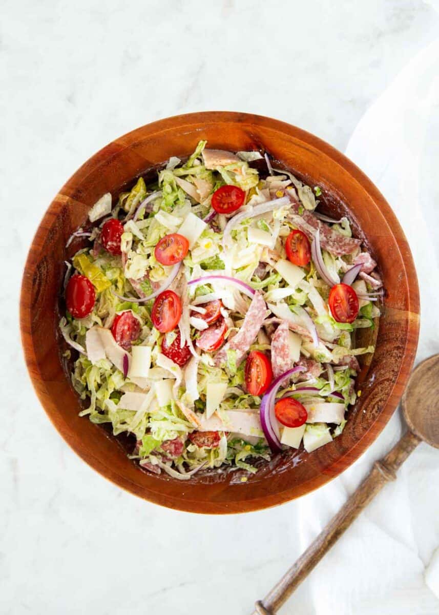 This Italian grinder salad takes the fresh flavors of my favorite sub sandwich and tosses them in a creamy, tangy dressing for an easy, low carb meal that’s deliciously filling. Overhead view of chopped Italian grinder salad with shredded lettuce, turkey, salami, provolone, red onion, and cherry tomatoes.