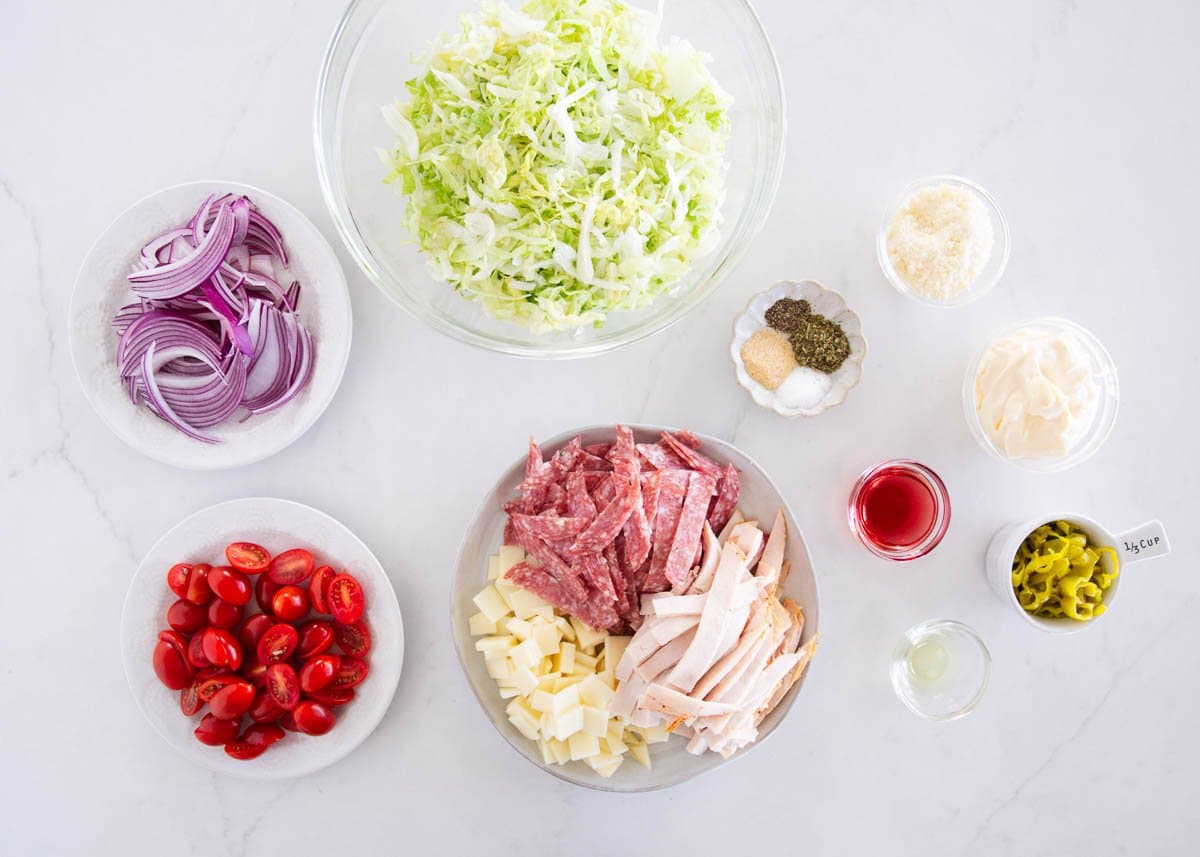 This Italian grinder salad takes the fresh flavors of my favorite sub sandwich and tosses them in a creamy, tangy dressing for an easy, low carb meal that’s deliciously filling. Ingredients for Italian grinder salad including shredded lettuce, turkey, salami, provolone, red onion, cherry tomatoes, and pepperoncini.