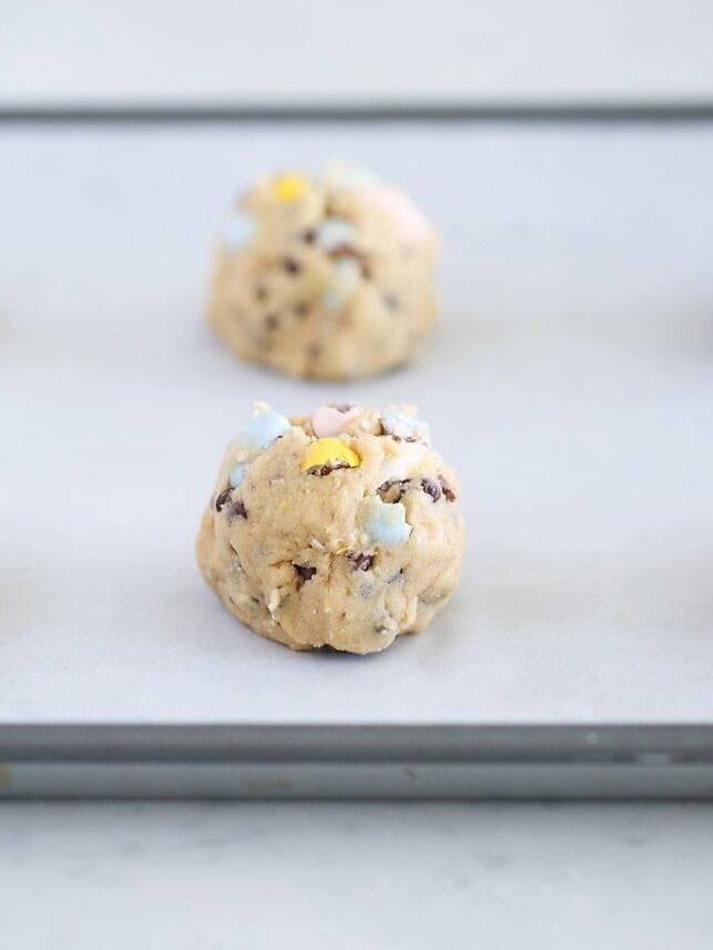 : Scoops of mini Cadbury egg cookie dough balls spaced on a baking sheet lined with parchment paper.
