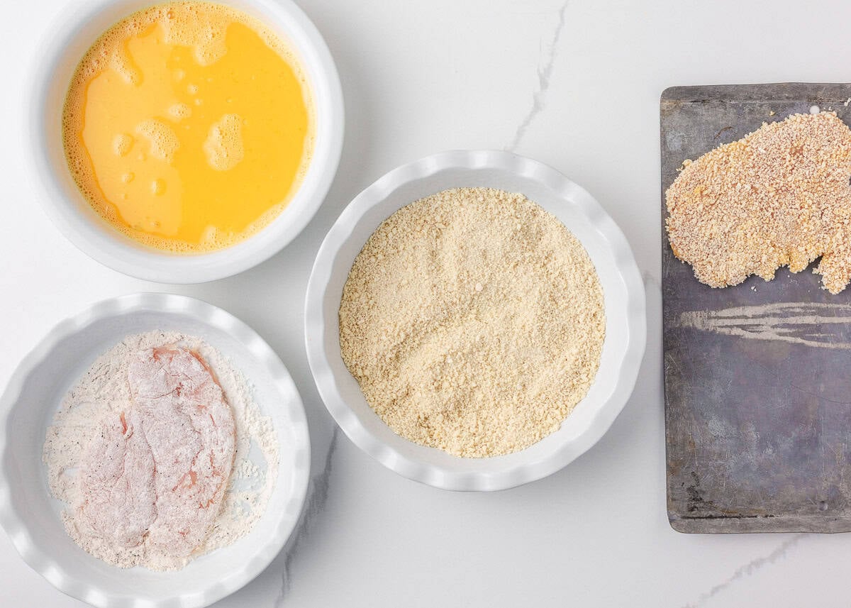 This chicken schnitzel is coated in seasoned breadcrumbs and pan fried until perfectly crispy, then finished with a squeeze of lemon. Thin, juicy, and ready in 30 minutes! Chicken schnitzel breading station with seasoned flour, beaten eggs, and panko breadcrumbs.