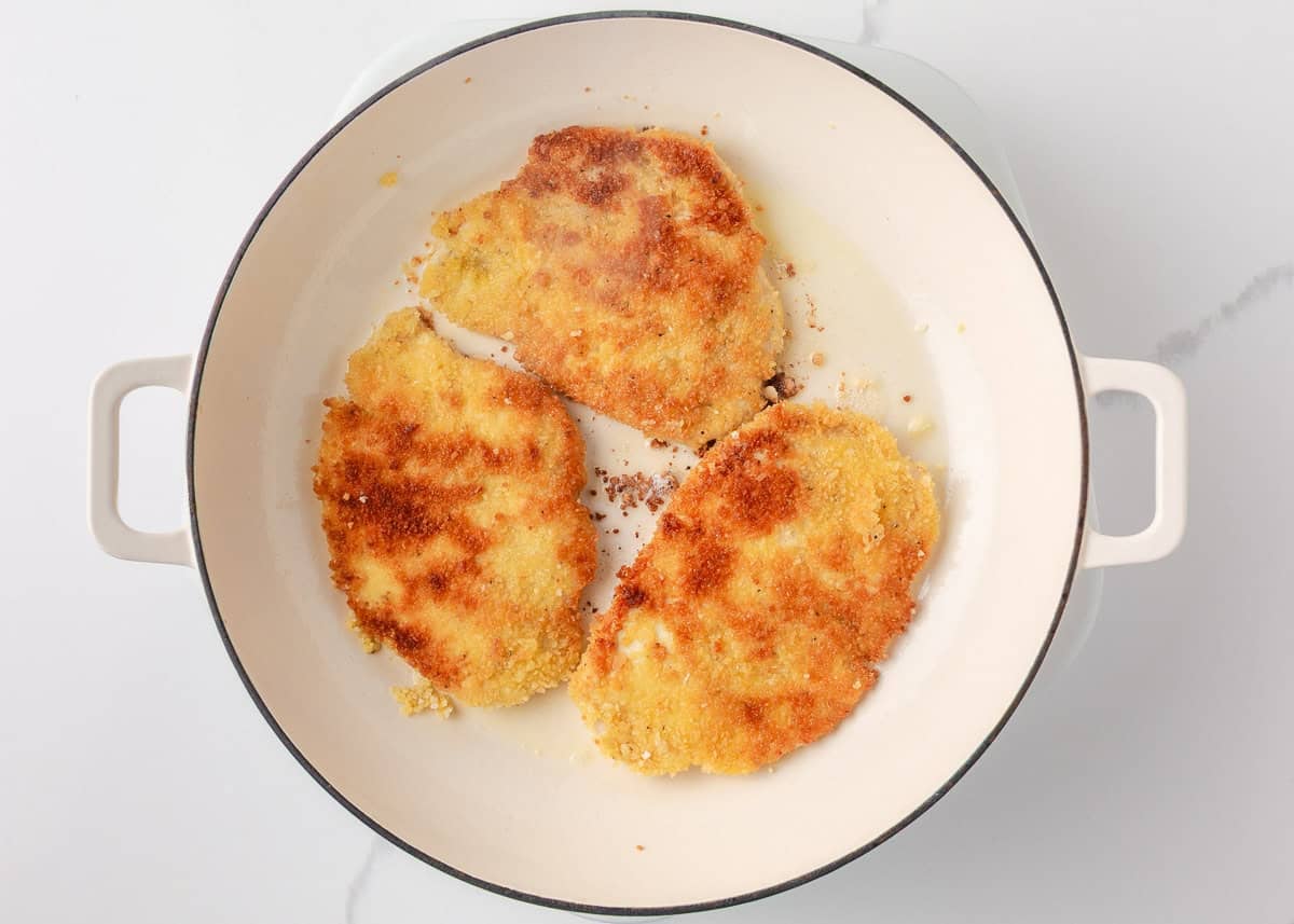 This chicken schnitzel is coated in seasoned breadcrumbs and pan fried until perfectly crispy, then finished with a squeeze of lemon. Thin, juicy, and ready in 30 minutes! Breaded chicken schnitzel cooking in a skillet until crispy and golden brown.