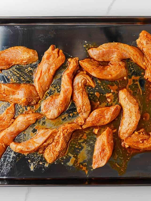 Colorful, fresh, and customizable, these chicken shawarma bowls are packed with bold spices, tender chicken, and all your favorite toppings. Marinated chicken arranged on a sheet pan before roasting.