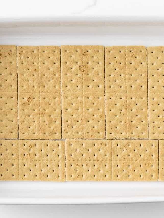 Bottom layer of graham crackers arranged in baking dish for no bake eclair cake with chocolate ganache.