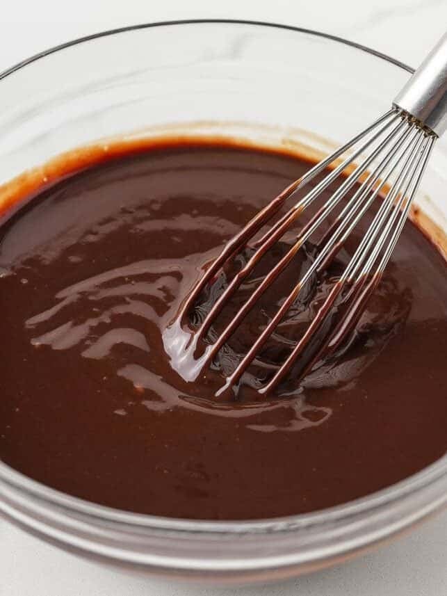 Homemade chocolate ganache being whisked in a glass bowl for eclair cake topping.