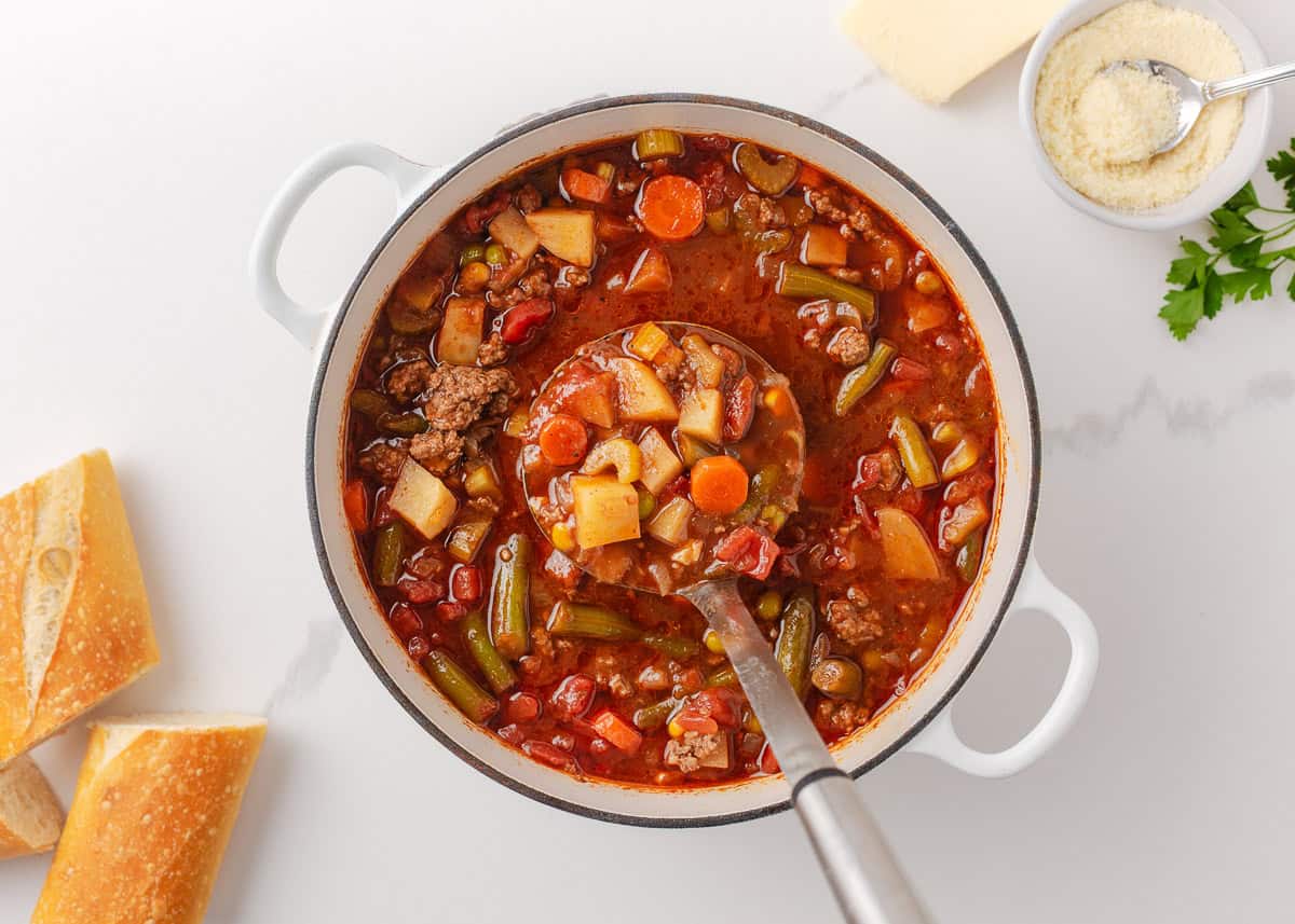 Hearty vegetable soup simmering in a Dutch oven with beef, potatoes, carrots, green beans, and tomatoes.