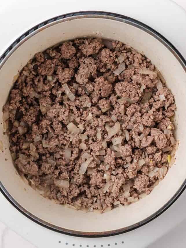 Ground beef and diced onion browned in a pot for vegetable soup.