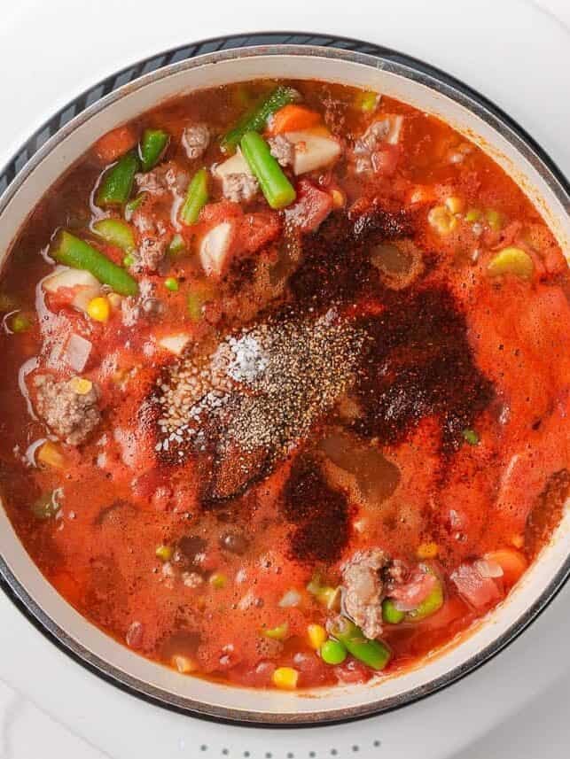 Seasonings added to hearty vegetable soup before stirring and simmering.