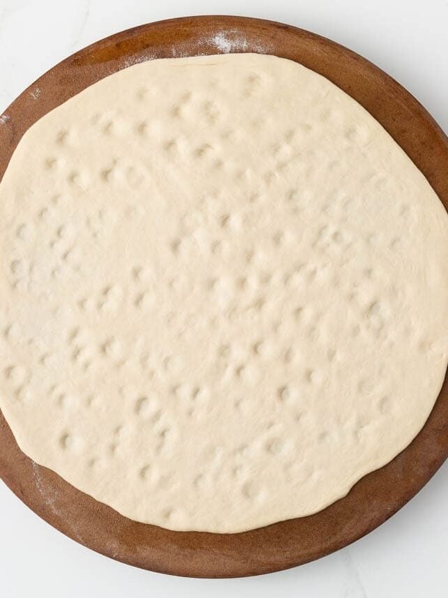 Pizza dough rolled out on pizza stone.
