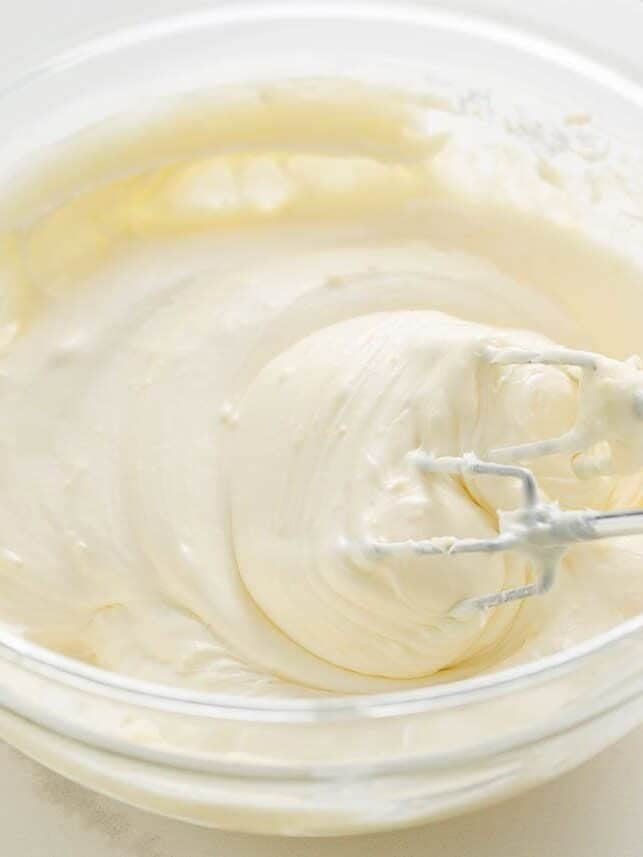 Lemon cream cheese frosting being whipped smooth with a hand mixer for lemon blueberry layer cake.