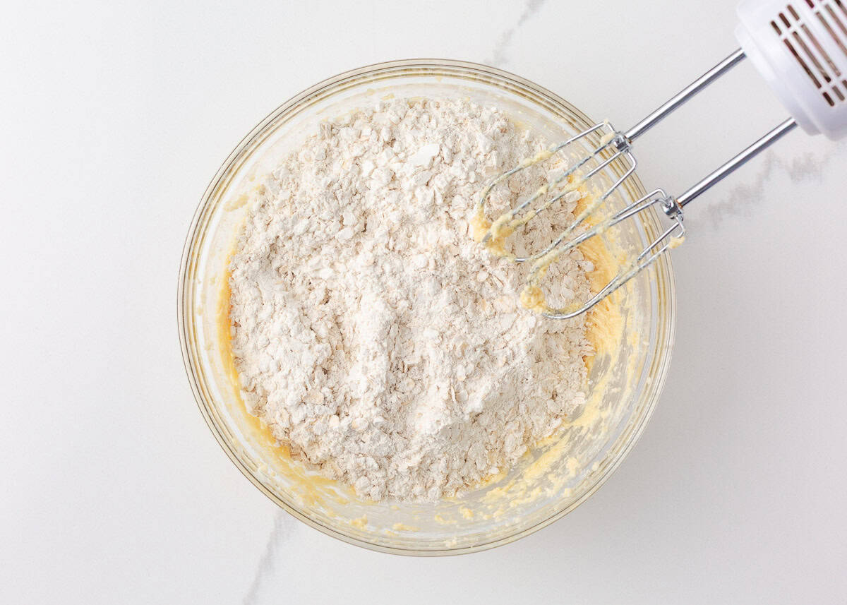 Loaded with oats, brown sugar, and melty chocolate chips, these oatmeal cookie bars are thick, chewy, and made in a single batch. No cookie scoop required! Dry ingredients being mixed into oatmeal cookie bar dough with a hand mixer.