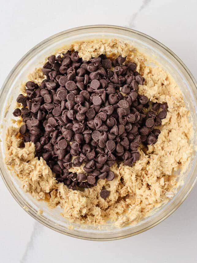 Loaded with oats, brown sugar, and melty chocolate chips, these oatmeal cookie bars are thick, chewy, and made in a single batch. No cookie scoop required! Chocolate chips added to oatmeal cookie bar dough in a mixing bowl.