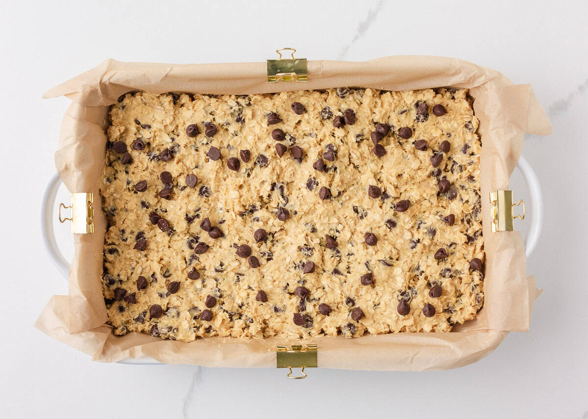 Loaded with oats, brown sugar, and melty chocolate chips, these oatmeal cookie bars are thick, chewy, and made in a single batch. No cookie scoop required! Oatmeal chocolate chip cookie bar dough pressed evenly into a parchment-lined baking dish.