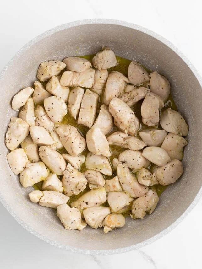 Chicken pieces sautéing in olive oil in a large pot.