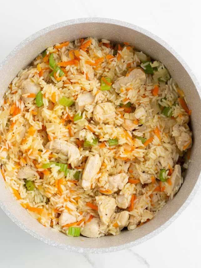 Cooked chicken and rice mixed with carrots and celery in a large pot.