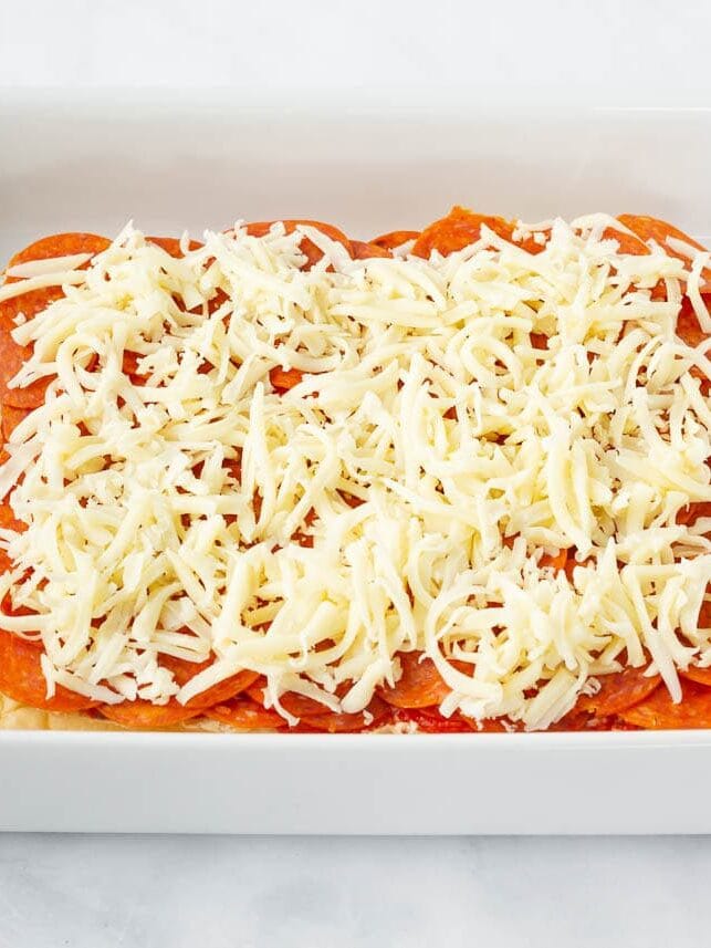 Shredded mozzarella cheese sprinkled over pepperoni on Hawaiian rolls.