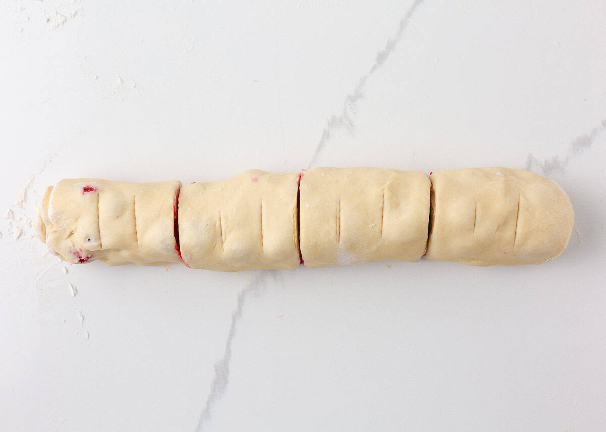These raspberry sweet rolls are an indulgent breakfast treat made with soft yeast dough, a swirled frozen raspberry filling, and thick cream cheese frosting! Rolling dough into a log to make raspberry sweet rolls.