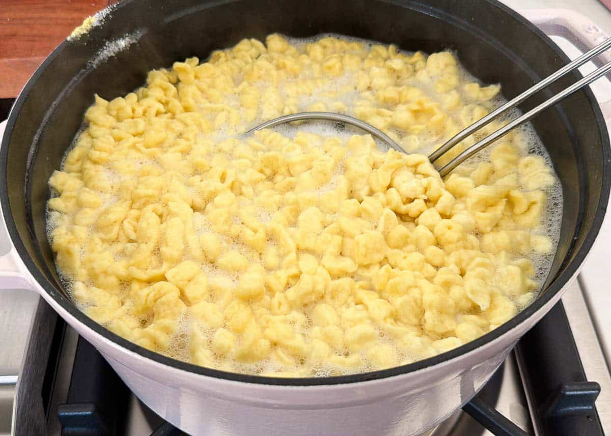 Learn to make homemade German spaetzle that's soft, chewy, and on the table in under 30 minutes. So good with brown butter, gravy, or cheese. German spaetzle boiling in a pot of salted water with a slotted spoon lifting the pasta.