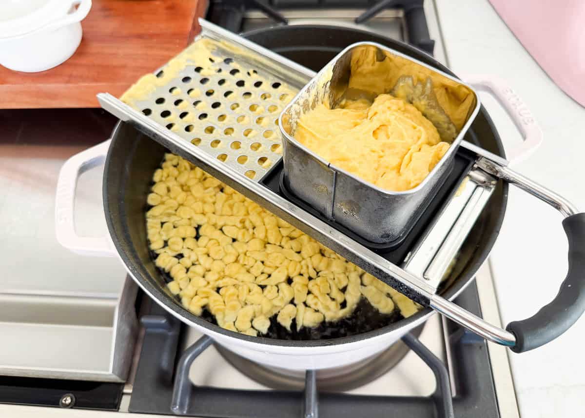 Learn to make homemade German spaetzle that's soft, chewy, and on the table in under 30 minutes. So good with brown butter, gravy, or cheese. Spaetzle dough being pressed through a spaetzle maker into a pot of simmering water.