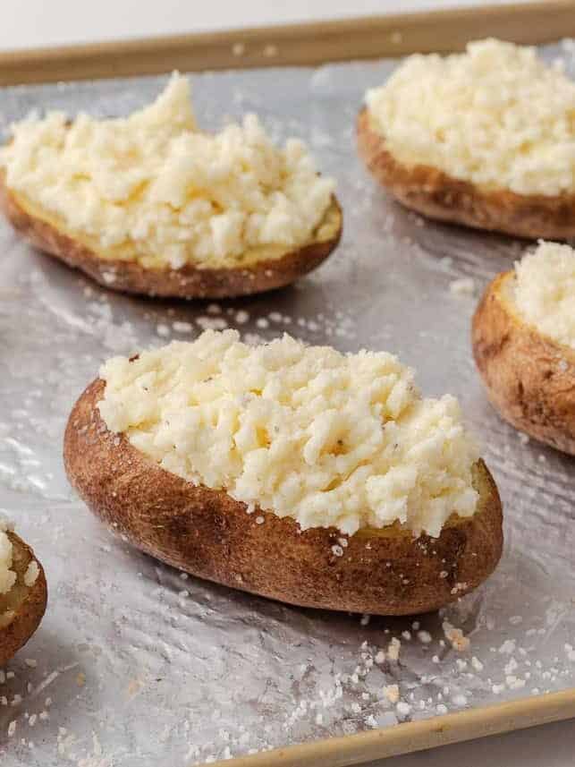 Potato skins filled with creamy mashed potato mixture arranged on a foil lined baking sheet.