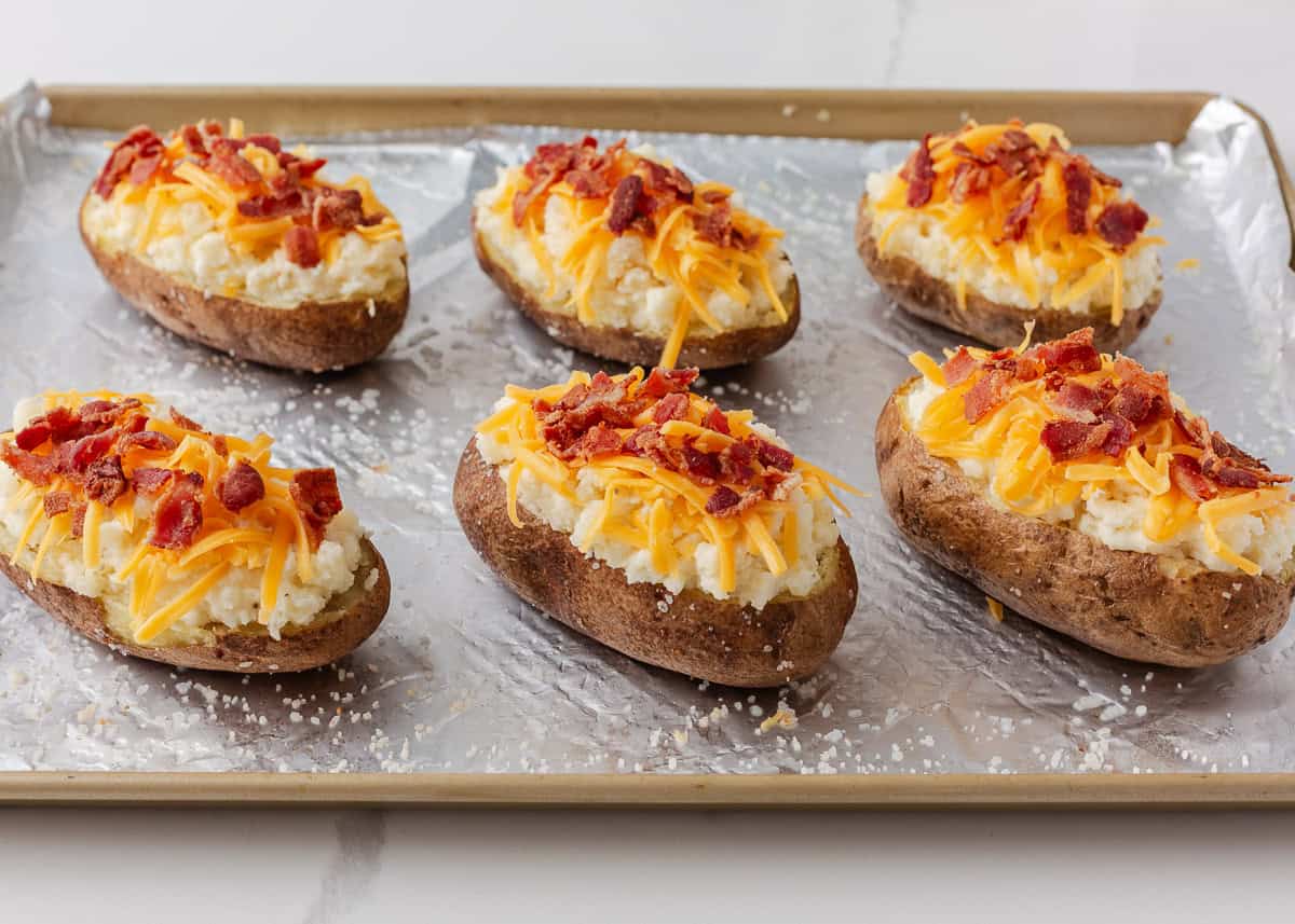 Twice baked potatoes topped with shredded cheddar cheese and crumbled bacon before the second bake.